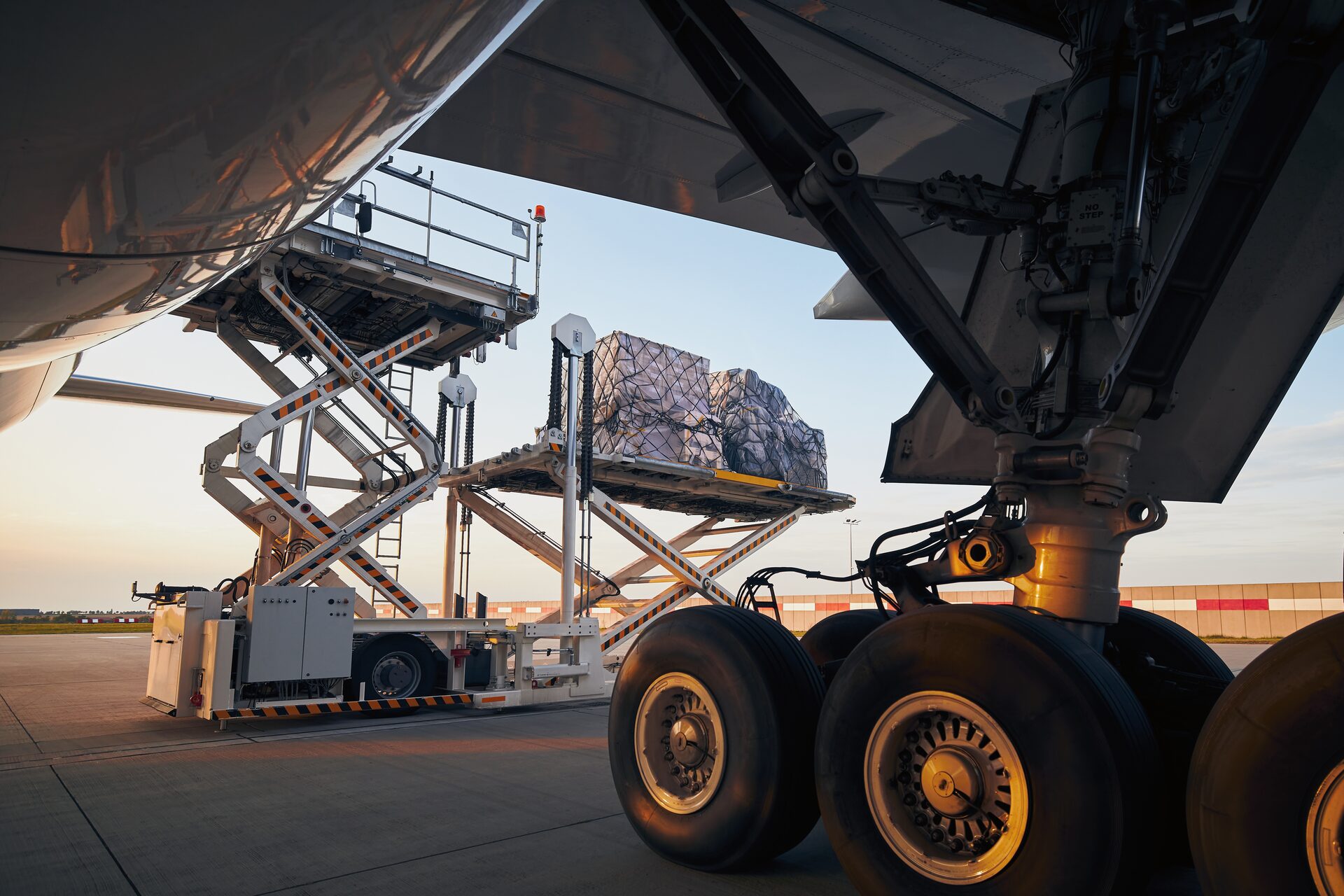 Airport high-loader raising netted air cargo towards an aircraft hold at sunset